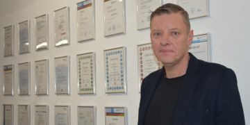 Geschäftsführer Holger Mylius vor der unternehmensinternen "Wall of Fame": Im Gang des Betriebsgebäudes werden die Abschlüsse, Qualifizierungen und Erfolge der Mitarbeitenden für alle sichtbar präsentiert. Ein Ansporn für alle, die auf dieser Wand noch nicht vertreten sind, HWK Cottbus/Veronika Martin