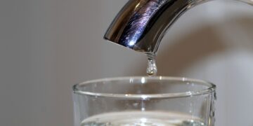 Letzter Tropfen an einem Wasserhahn ueber einem Glas als Symbol fuer die unterbrochene Trinkwasserversorgung