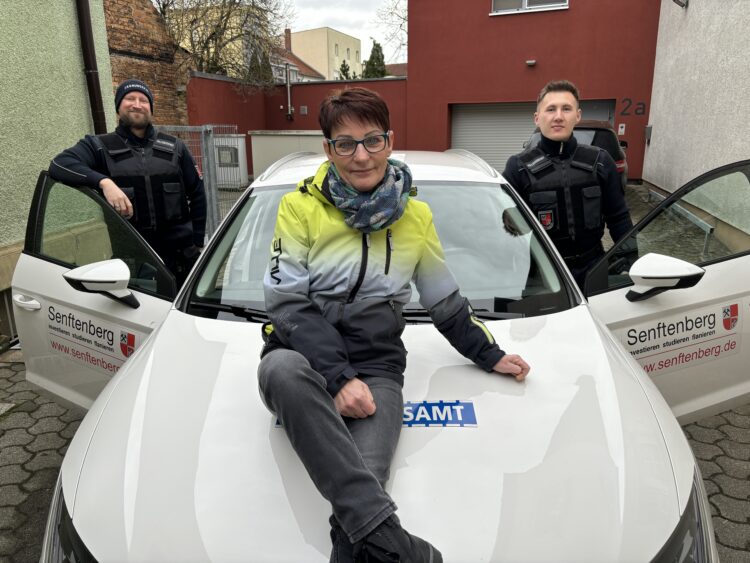 Mit dem weißen Dienstauto war Marina Tietze viel unterwegs. Wenngleich sie durchs Stadtgebiet am liebsten zu Fuß patrouillierte. Zum Abschied nahmen Sachgebietsleiter Tillmann Bartz (r.) und ihr Nachfolger Torsten Manthey ihre Kollegin nochmal in die Mitte. (Bild: Andrea Budich)