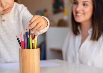 Little preschooler kid drawing with coloured pencils with mother or teacher educator. Focus on the pencils. Homeschooling. Learning community. Montessori school.