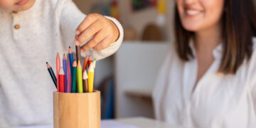 Little preschooler kid drawing with coloured pencils with mother or teacher educator. Focus on the pencils. Homeschooling. Learning community. Montessori school.