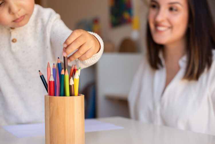 Little preschooler kid drawing with coloured pencils with mother or teacher educator. Focus on the pencils. Homeschooling. Learning community. Montessori school.