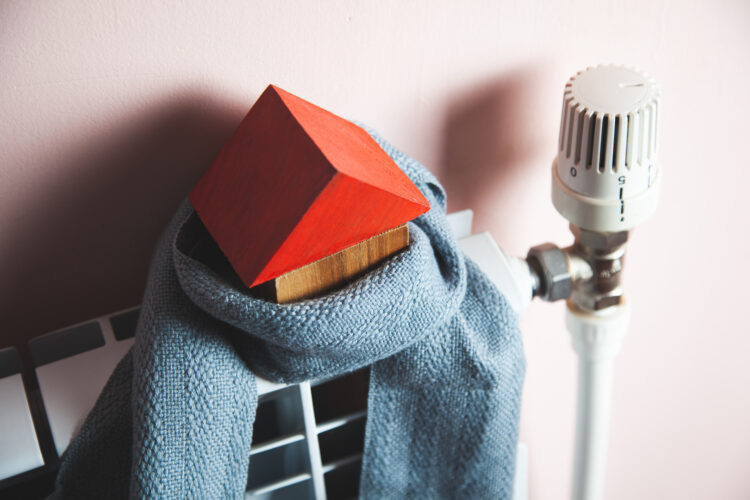 Model of a house in a scarf on a radiator indoors. Winter heating efficiency