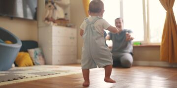baby first steps. baby goes her father at window learns to walk to take first steps. happy family kid dream concept. dad calls son baby first steps indoors. happy family lifestyle indoors concept