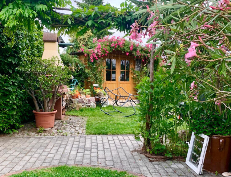 Blühendes Gartenparadies mit dichter Bepflanzung im Vordergrund und einer Laube im Hintergrund – ein stimmungsvoller Einblick in die Vielfalt privater Gartenkultur im Elbe-Elster-Land. (Bild: Carola Salzer)