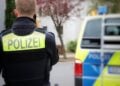 Polizist mit Funkgerät vor einem Wohnhaus, daneben ein Streifenwagen