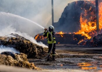 Feuerwehrmann bekämpft die Flammen am brennenden Strohlager in Großkmehlen