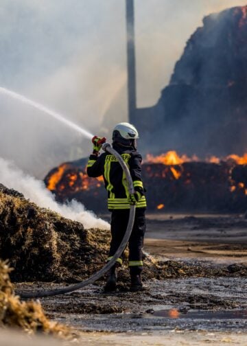 Feuerwehrmann bekämpft die Flammen am brennenden Strohlager in Großkmehlen