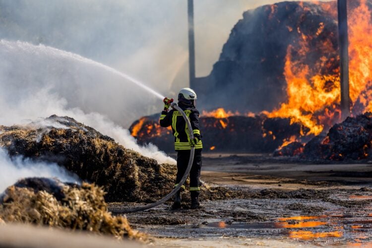 Feuerwehrmann bekämpft die Flammen am brennenden Strohlager in Großkmehlen