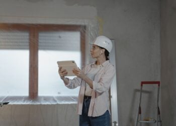 Planerin mit Schutzhelm prüft auf einer Baustelle Unterlagen auf einem Tablet