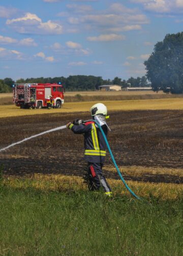 Feuerwehrmann mit Strahlrohr am Feldrand