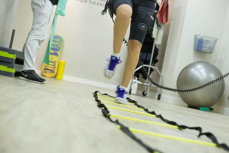 Patient mit Knieorthese trainiert in einer Physiotherapiepraxis an einer Koordinationsleiter