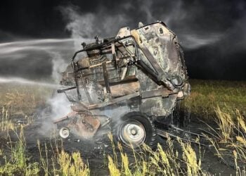 Ausgebrannte Ballenpresse auf einem Feld wird nachts von einem Löschwasserstrahl abgelöscht