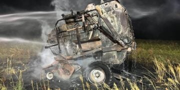 Ausgebrannte Ballenpresse auf einem Feld wird nachts von einem Löschwasserstrahl abgelöscht