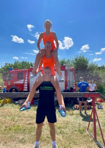 Feuerwehrsportler zeigen eine Hebefigur vor dem Löschfahrzeug