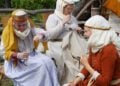 Drei Frauen in mittelalterlicher Kleidung nähen von Hand und spinnen Fäden mit einer Spindel