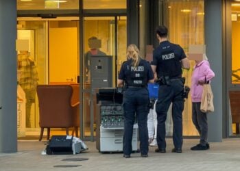 Zwei Polizisten stehen vor dem Eingang eines Gebäudes, davor steht ein herausgetragenes Gerät