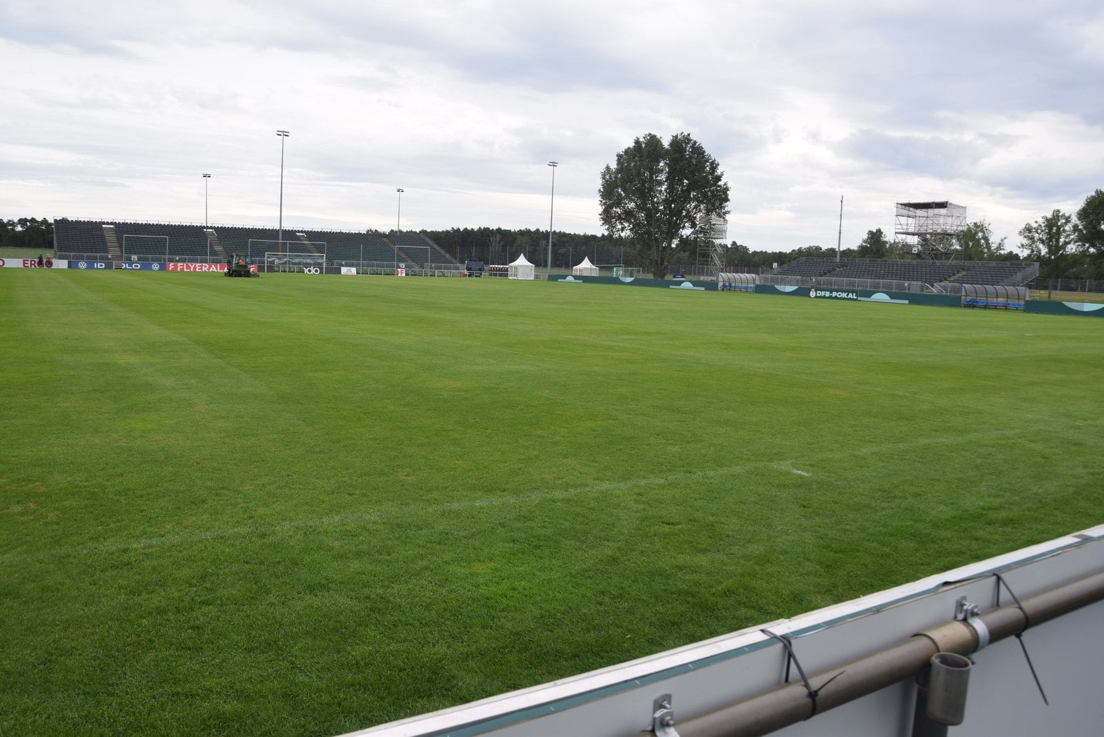 Weiter Blick über den Rasen des Sportparks, im Hintergrund Tribünen und ein Kameraturm