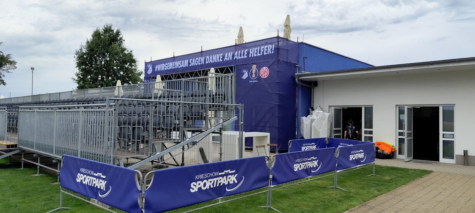 Blaues Zelt und Gerüsttribüne neben dem Vereinsgebäude, darüber ein Banner mit Dank an die Helfer