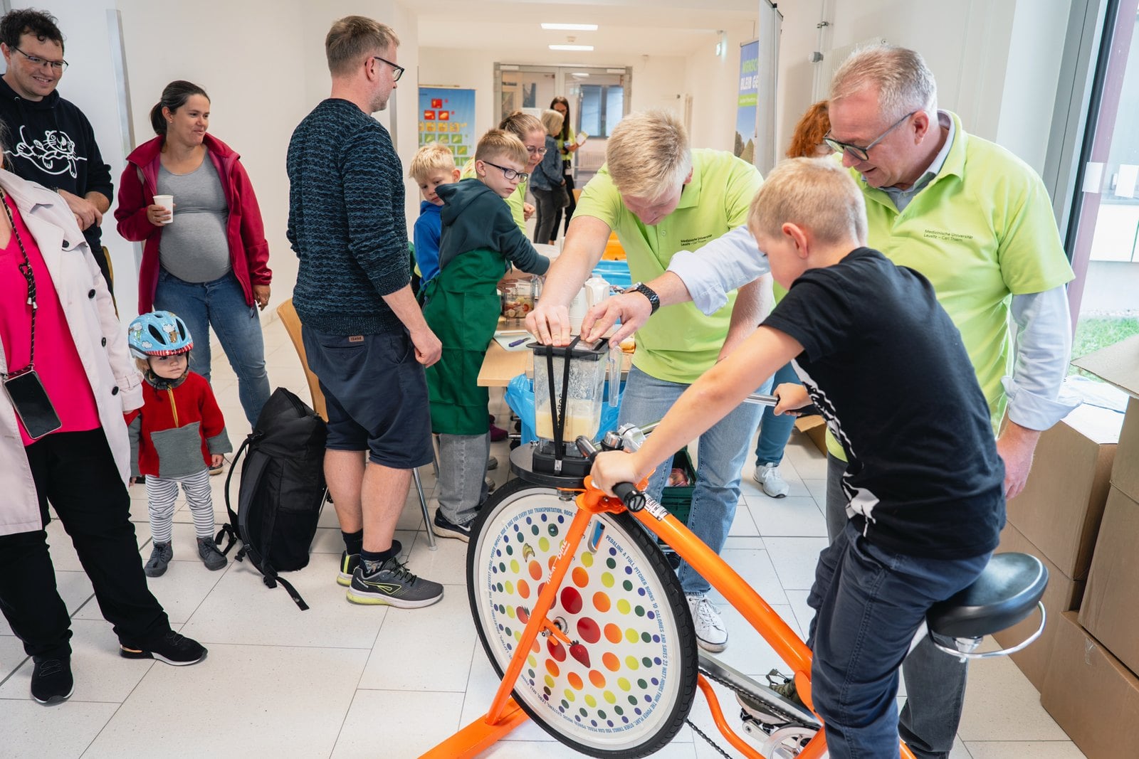 Kinder und Erwachsene an einem Smoothie-Fahrrad in einem Klinikfoyer