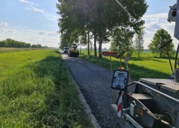 Baumaschine auf einem schmalen Radweg zwischen Feldern und Baumreihe