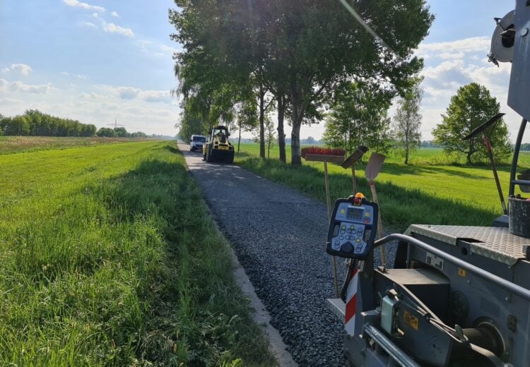 Baumaschine auf einem schmalen Radweg zwischen Feldern und Baumreihe