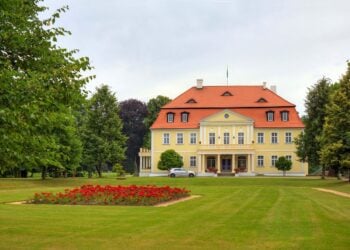 Gelbes klassizistisches Herrenhaus hinter einer Rasenfläche mit Blumenbeet
