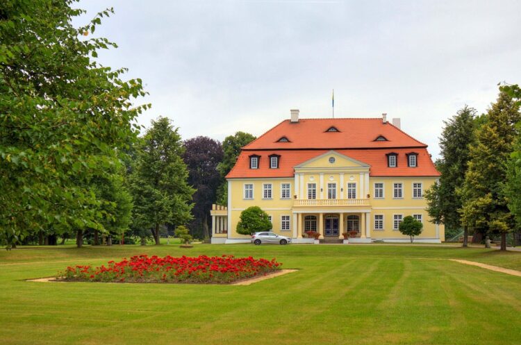 Gelbes klassizistisches Herrenhaus hinter einer Rasenfläche mit Blumenbeet