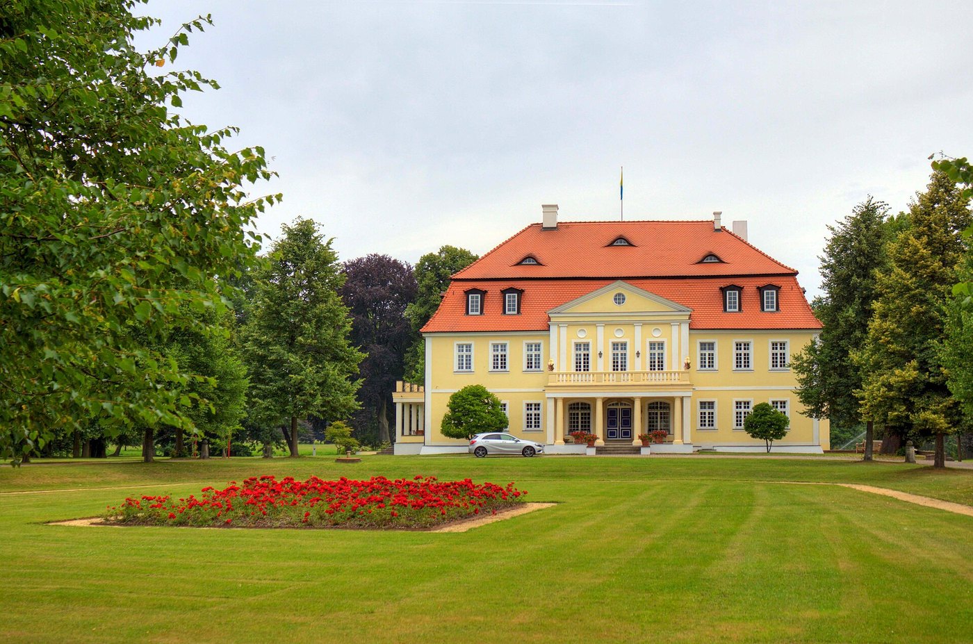 Gelbes klassizistisches Herrenhaus hinter einer Rasenfläche mit Blumenbeet