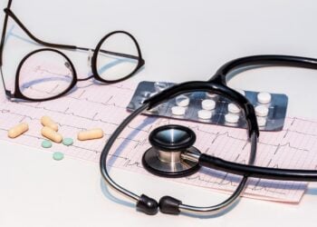 Ein EKG-Ausdruck mit Stethoskop, Brille und Tabletten auf einem Tisch