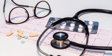 Ein EKG-Ausdruck mit Stethoskop, Brille und Tabletten auf einem Tisch