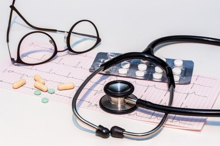 Ein EKG-Ausdruck mit Stethoskop, Brille und Tabletten auf einem Tisch