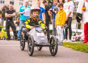 Ein Kind mit Helm steuert eine Seifenkiste an Zuschauern vorbei