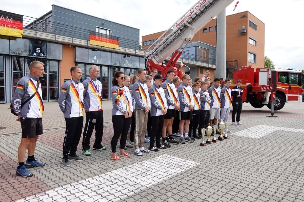 Sportlerinnen und Sportler stehen in einer Reihe vor der Feuerwache