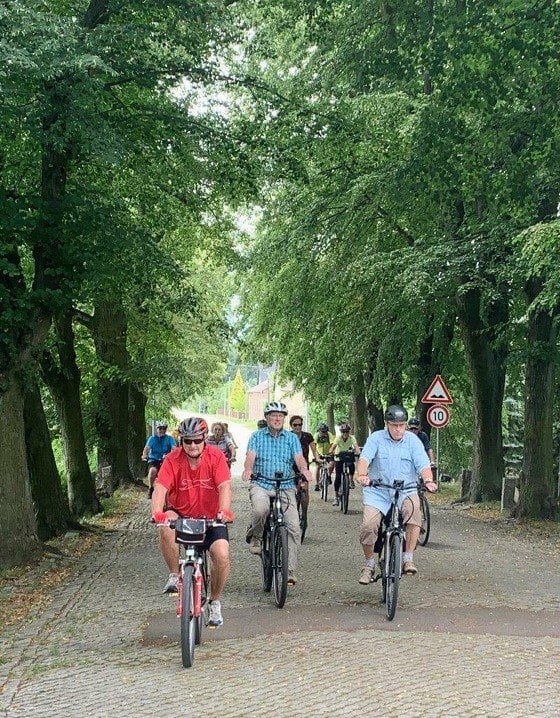 Gruppe von Radfahrern auf einer von Bäumen gesäumten Allee