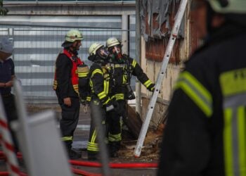 Feuerwehrleute unter Atemschutz vor einem Gebäude, daneben eine angelehnte Leiter