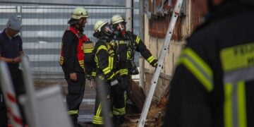Feuerwehrleute unter Atemschutz vor einem Gebäude, daneben eine angelehnte Leiter
