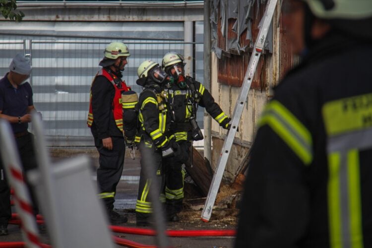 Feuerwehrleute unter Atemschutz vor einem Gebäude, daneben eine angelehnte Leiter