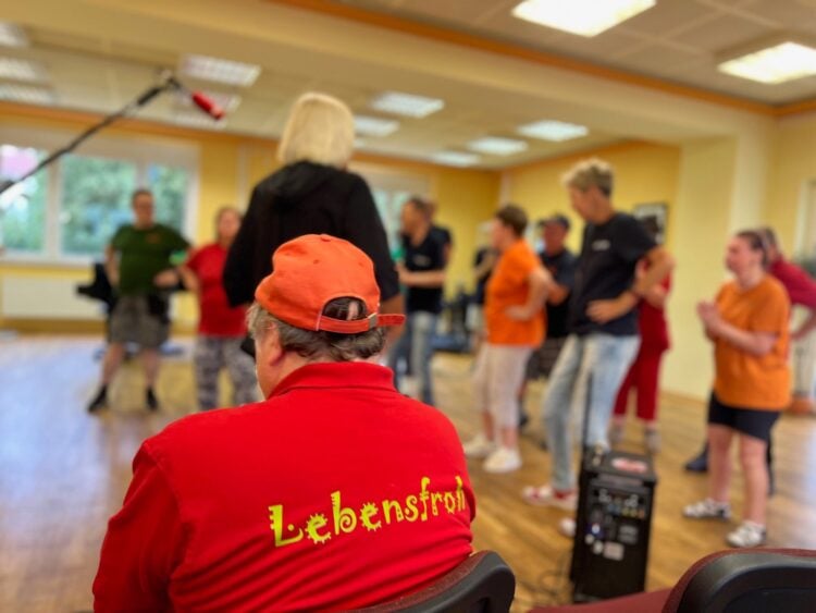 Probenraum mit Mitgliedern der Gruppe Lebensfroh, im Vordergrund ein rotes Shirt mit dem Schriftzug Lebensfroh