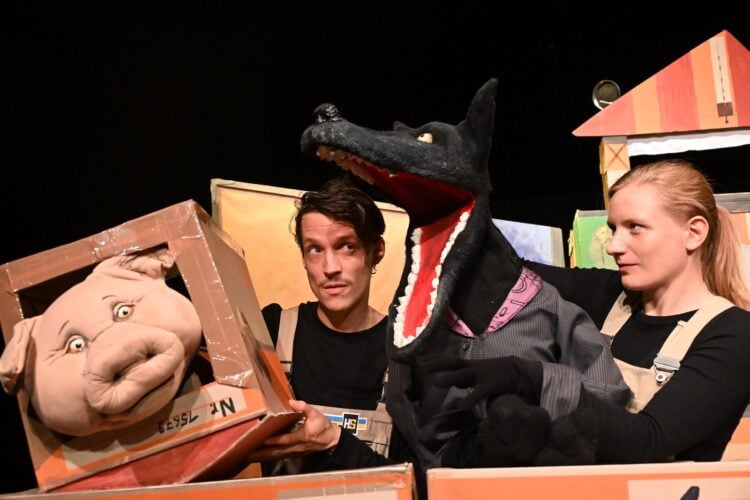 Zwei Spieler fuehren eine Wolfspuppe und eine Schweinepuppe zwischen Pappkartons