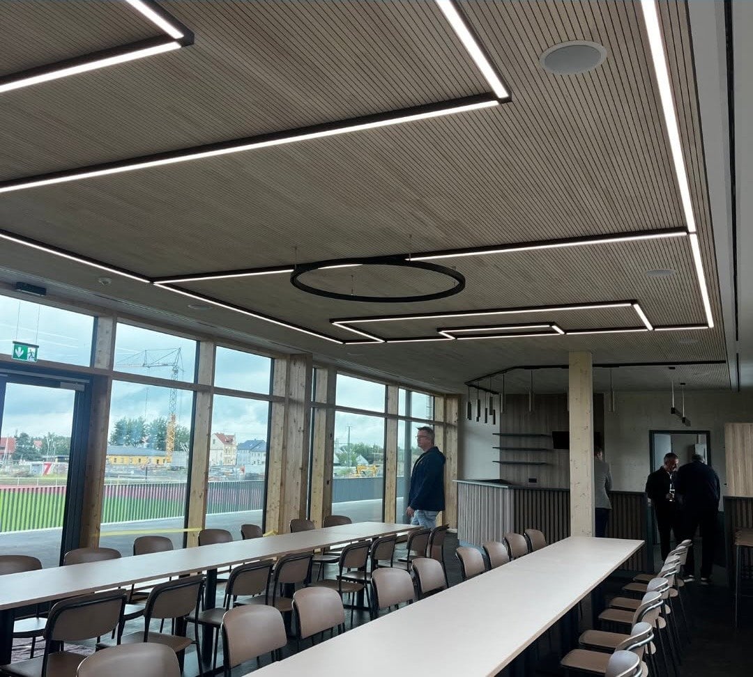 Langer Tisch mit Stühlen in einem Raum mit Holzdecke und Fensterfront zum Sportplatz