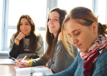 Drei Frauen sitzen an einem Tisch in einem hellen Raum und arbeiten mit Unterlagen
