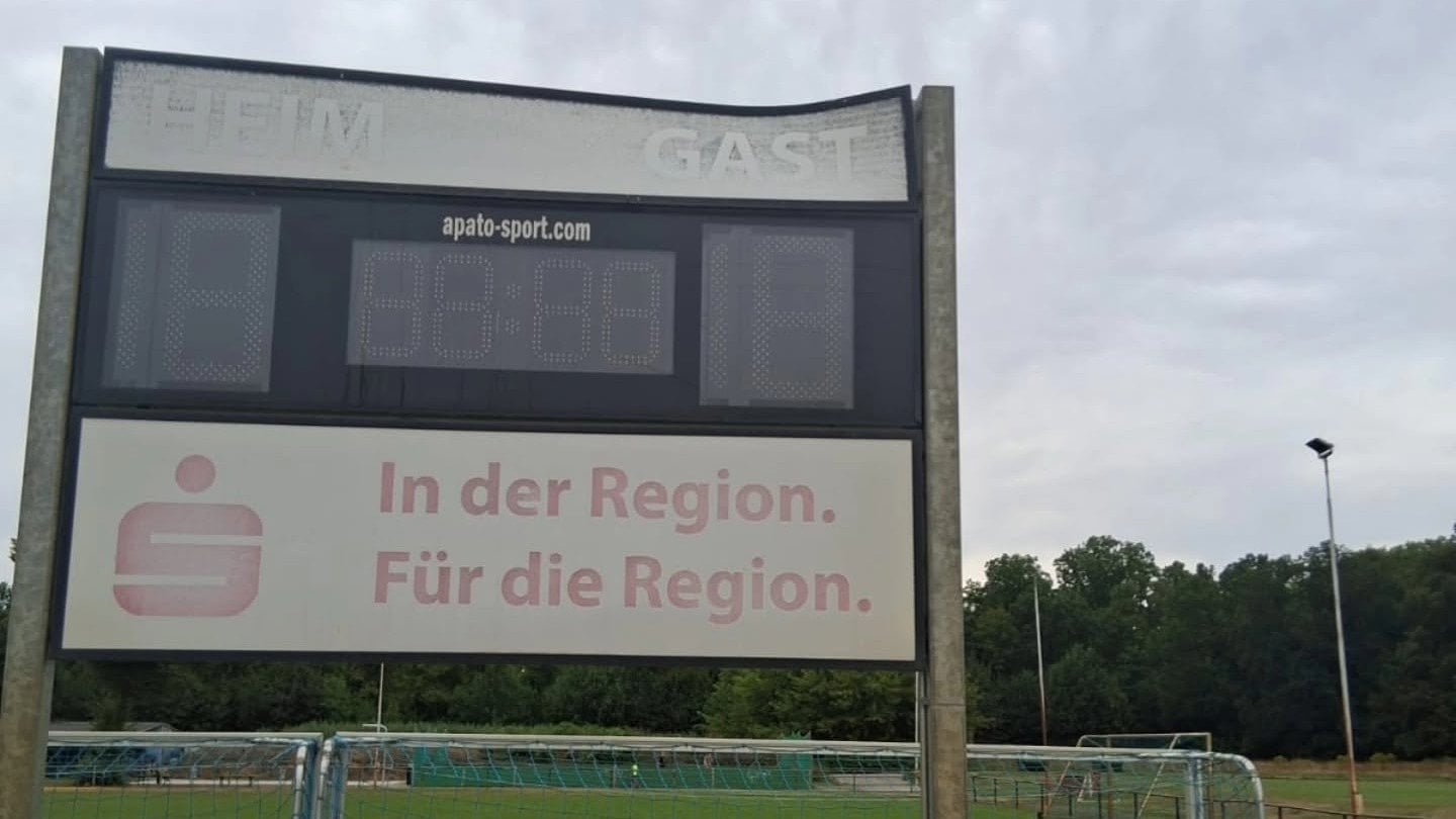 Anzeigetafel mit der Aufschrift Heim und Gast am Rand des Sportplatzes