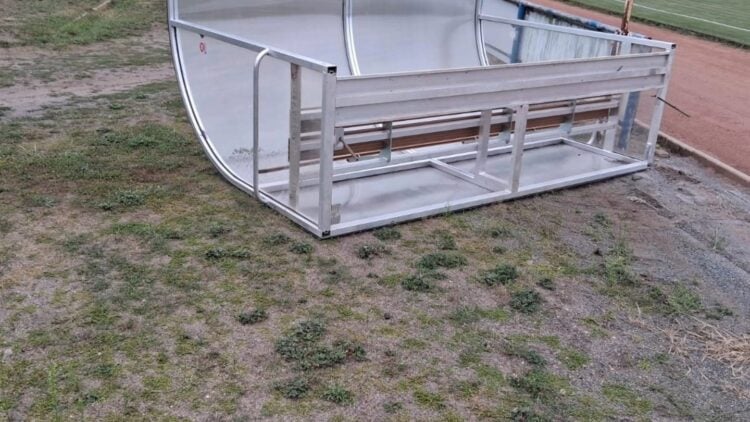 Umgekippter Spielerunterstand aus Metall und Kunststoff neben dem Sportplatz