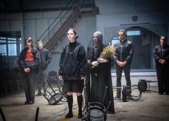 Linn Reusse als Hamlet im Hoodie inmitten des Ensembles im Hangar 1 in Cottbus
