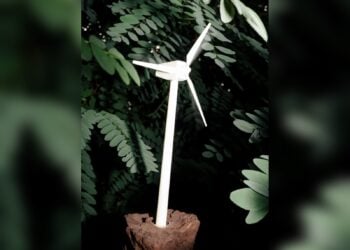 Modell eines Windrads steckt in einem Stück Braunkohle vor grünem Laub