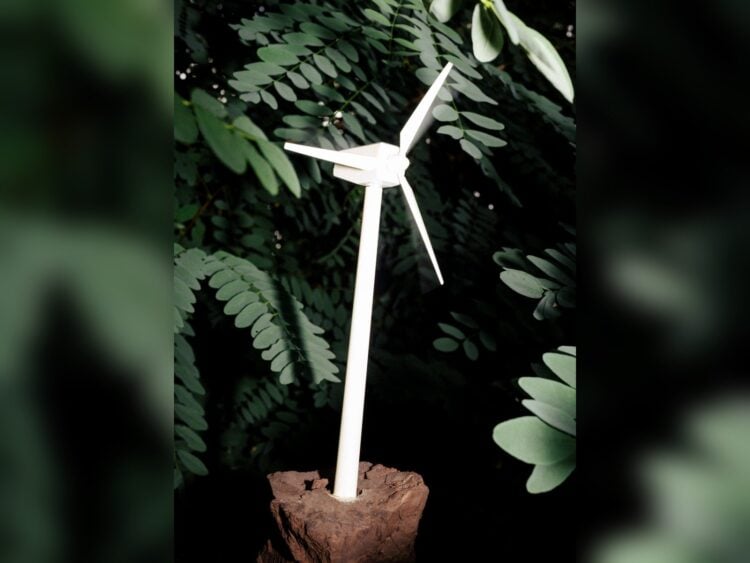 Modell eines Windrads steckt in einem Stück Braunkohle vor grünem Laub