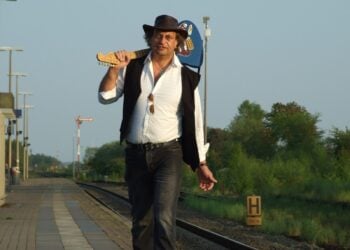 Martin Storm mit Gitarre über der Schulter auf einem Bahnsteig