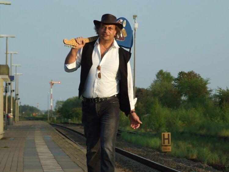 Martin Storm mit Gitarre über der Schulter auf einem Bahnsteig