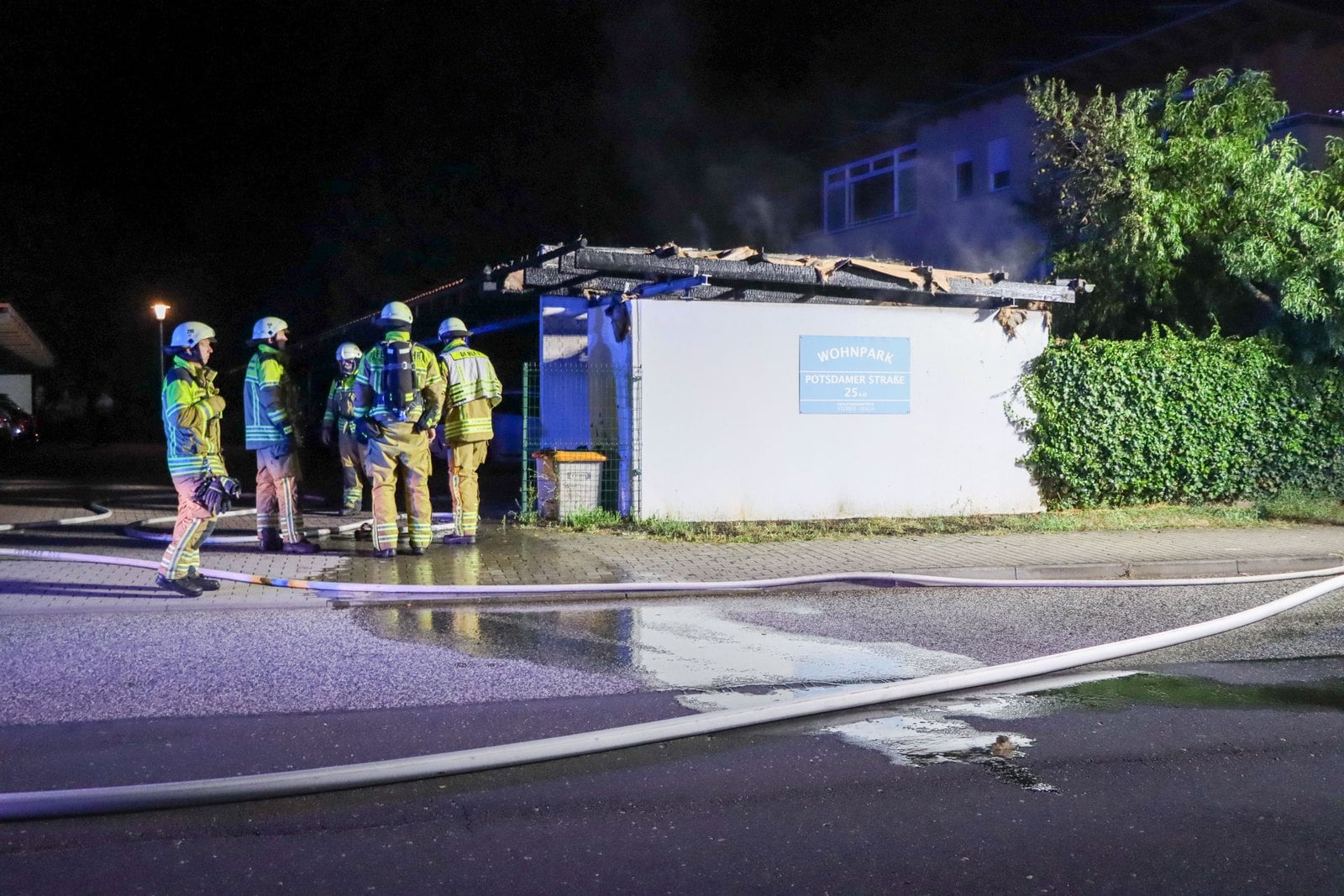 Einsatzkräfte vor dem ausgebrannten Carport nach dem Löschen